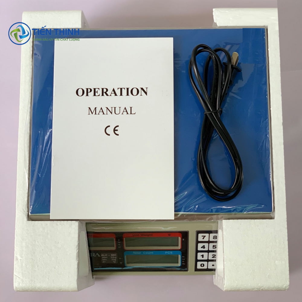 Cân điện tử màu xanh với sách hướng dẫn sử dụng và dây nguồn.