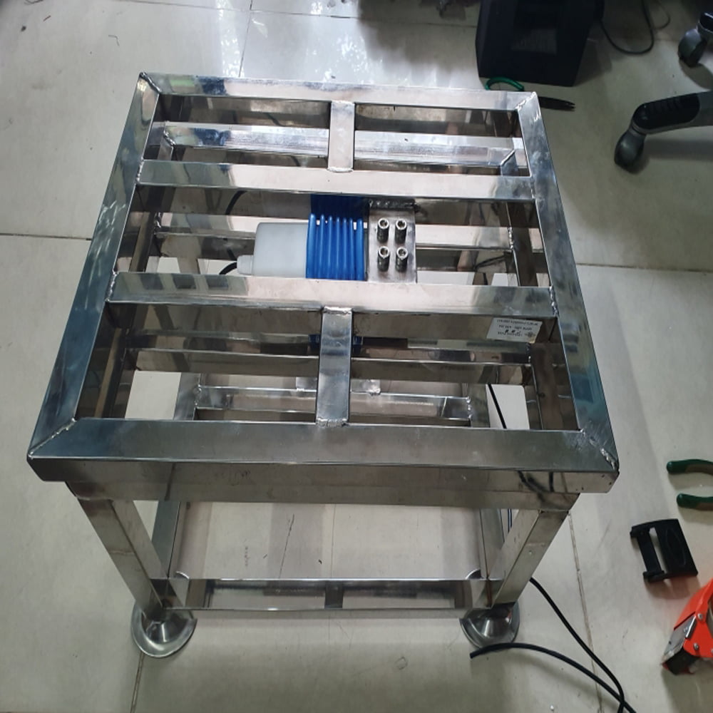 Khung kim loại vuông vức, gắn thiết bị màu xanh, có bánh xe lăn.