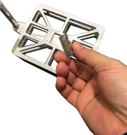 Bàn tay đang giữ một bộ phận kim loại màu bạc có cấu trúc phức tạp.