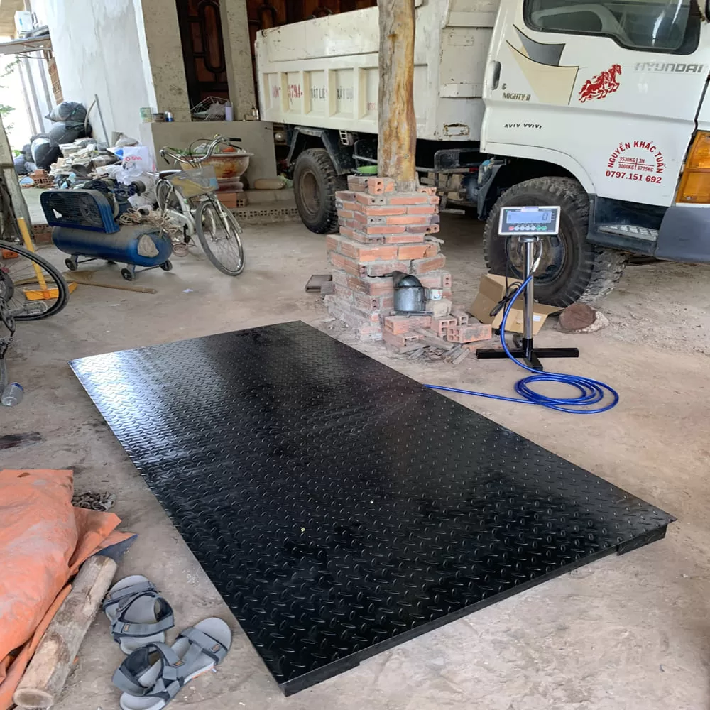 Cân điện tử đen đặt trước xe tải Hyundai, có đồ dùng cá nhân gần đó.