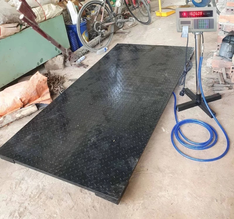 Cân điện tử đang đo một tấm kim loại màu đen hình chữ nhật lớn.