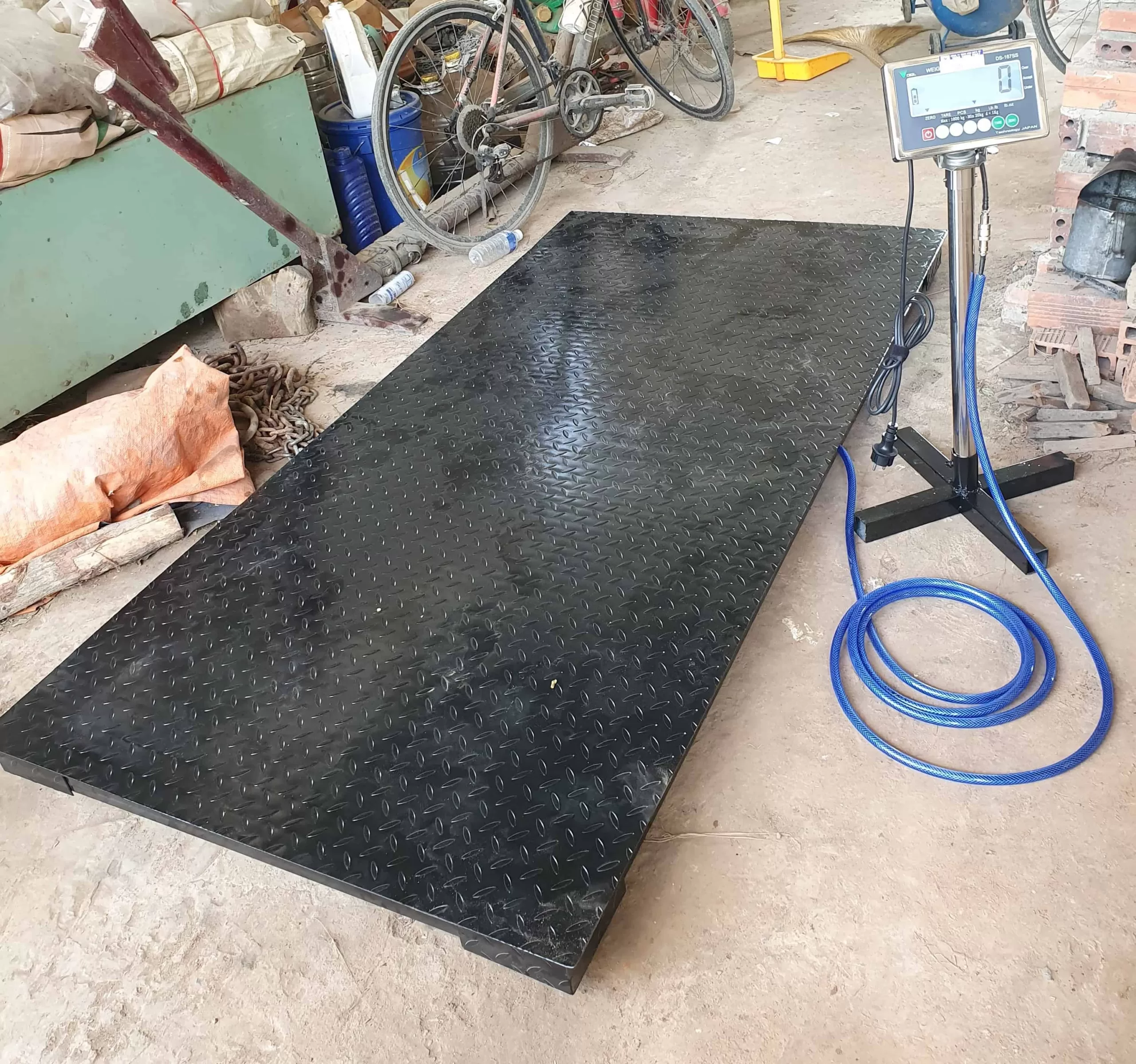 Cân điện tử công nghiệp đặt trên nền xưởng, đo khối lượng hàng hóa.