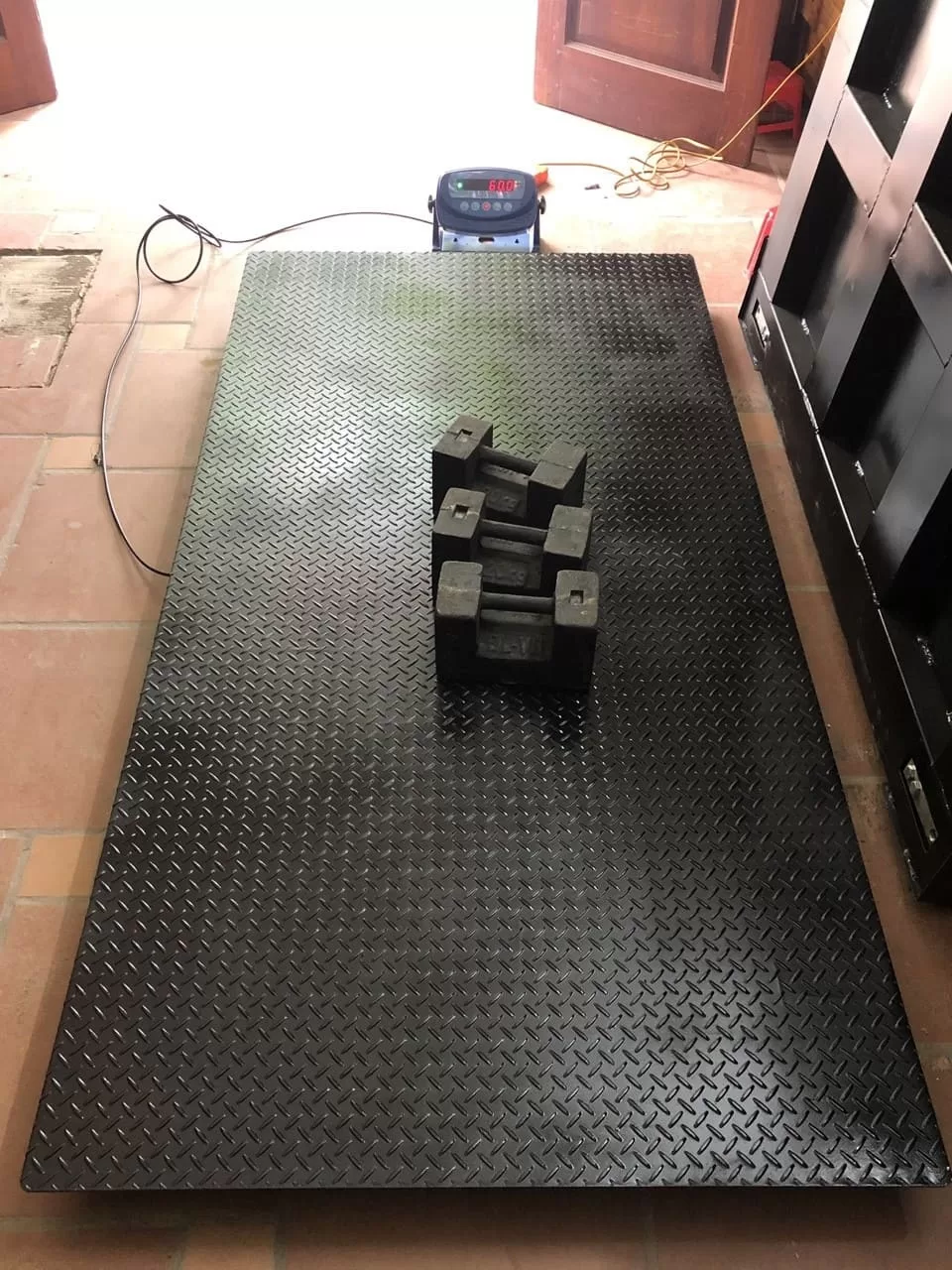 Cân điện tử lớn đang đo khối lượng tạ đĩa màu đen.