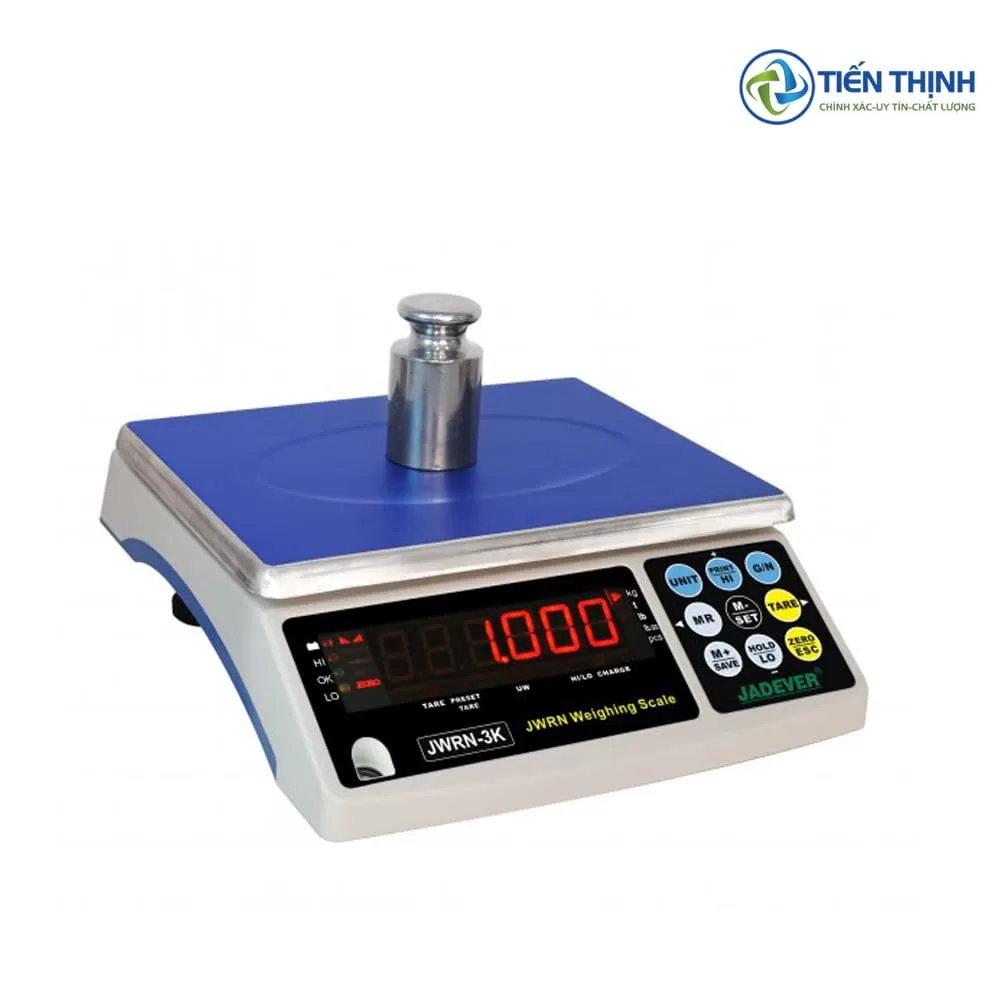 Cân điện tử Jadever trắng bạc với vật nặng, màn hình hiển thị số rõ ràng.