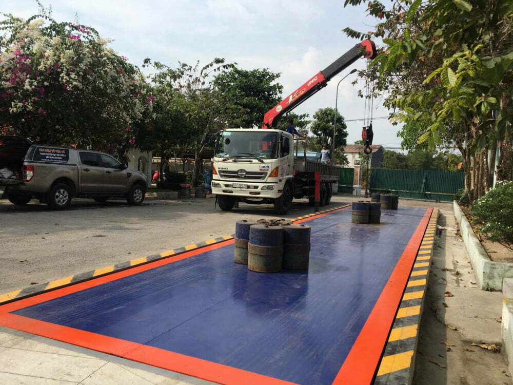 Xe tải cẩu đang hạ hàng xuống bãi cân, có nhiều thùng phuy.