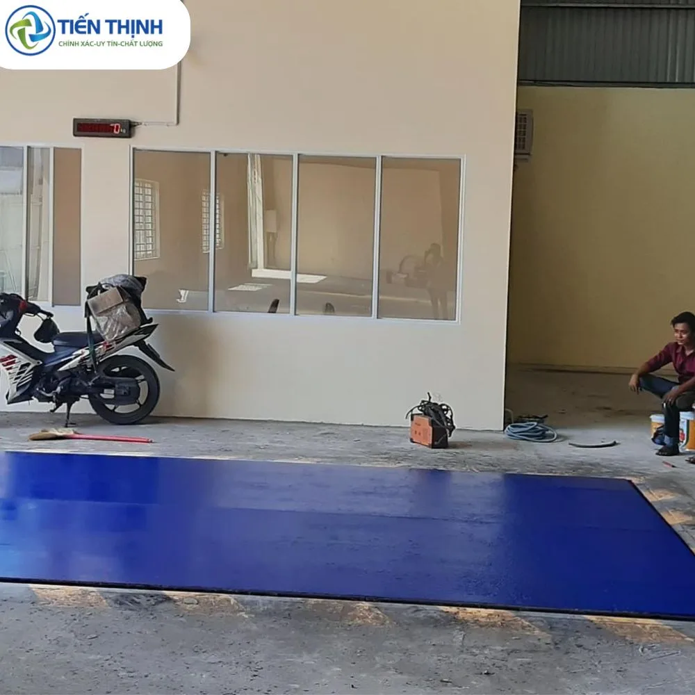 Sân nhà kho được sơn màu xanh lam nổi bật, có xe máy và người ngồi.