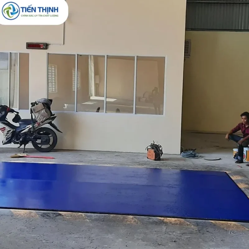 Sân nhà kho được sơn màu xanh lam nổi bật, có xe máy và người ngồi.